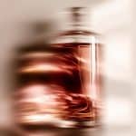 Flacon de parfum aux reflets bordeaux et ambrés dans une mise en scène artistique, illustrant l'univers sensoriel d'un studio de branding beauté et bien-être à Lyon